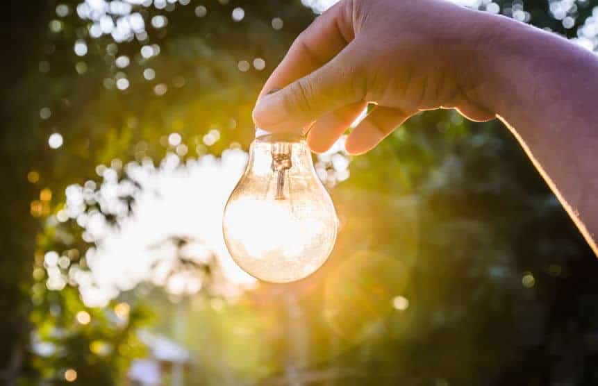 hand holding a lightbulb in front of sun while it's setting