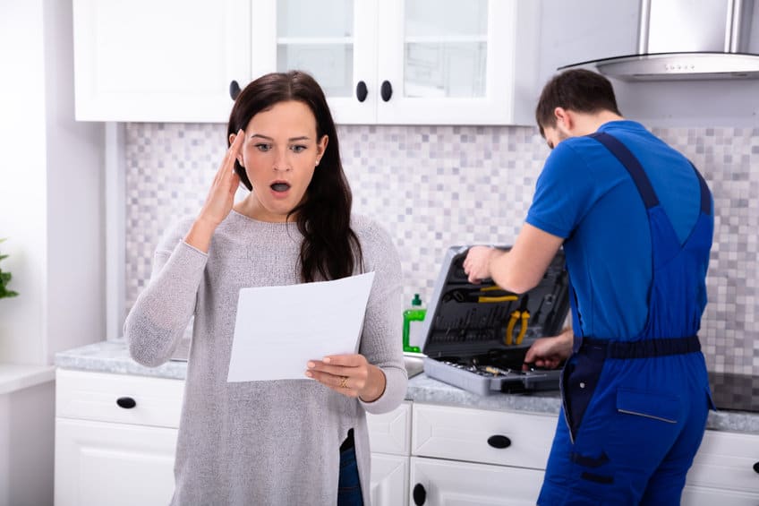 young homeowner with a shocked face while reading repair cost estimate with technician closing up his tools behind her