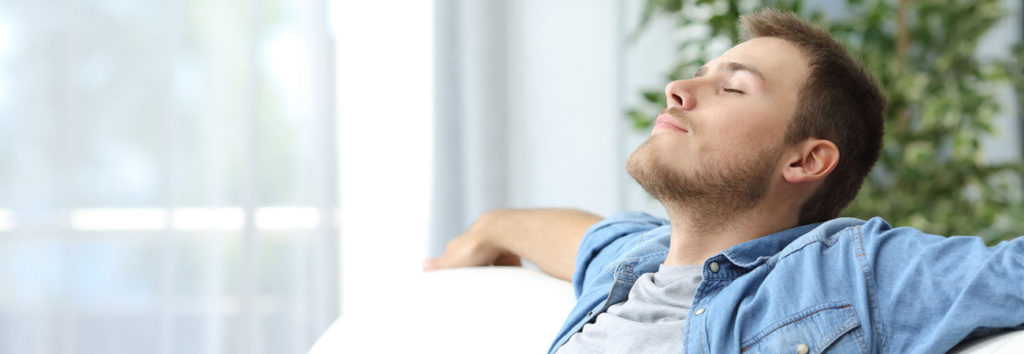 man relaxing on his couch with his head back and eyes closed enjoying clean air