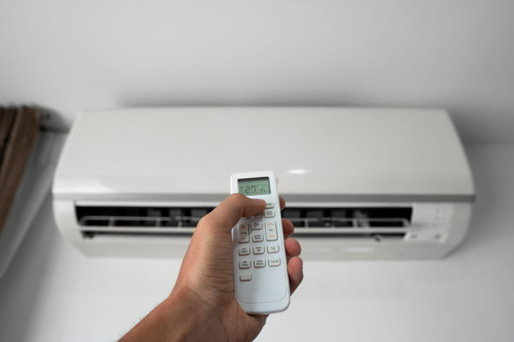 Hand holding remote control and adjusting temperature of air conditioner mounted on a white wall