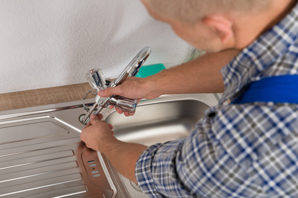 Male Plumber Fixing Faucet In Kitchen Sink At Home