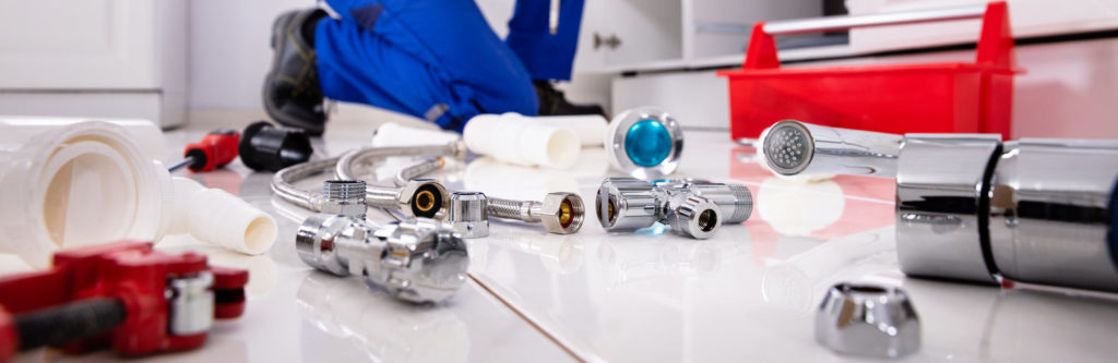 Plumber Tools And Equipment On Floor In Kitchen With Plumber Installing The Sink At Background