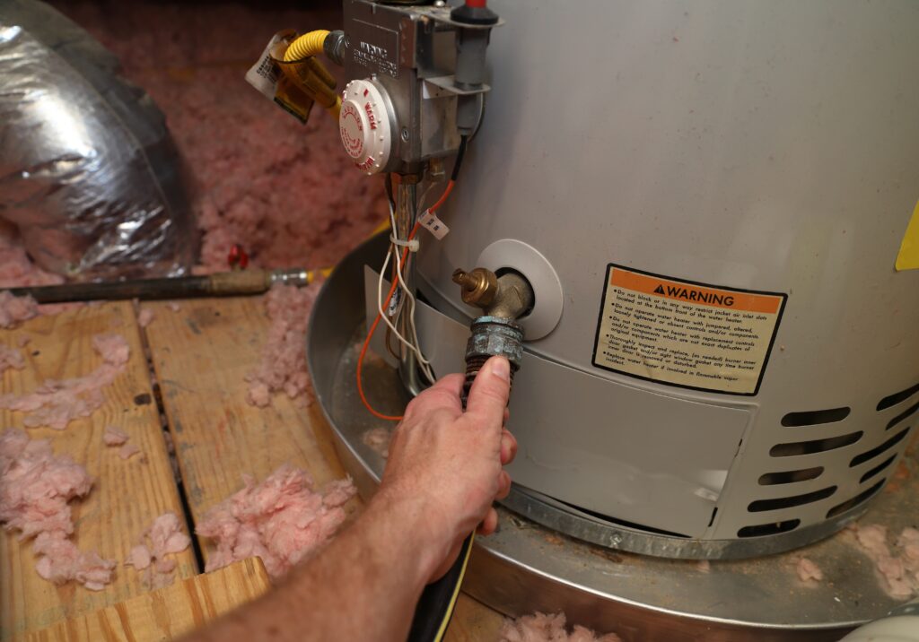 technician hand reaching down to repair tanked water heater system